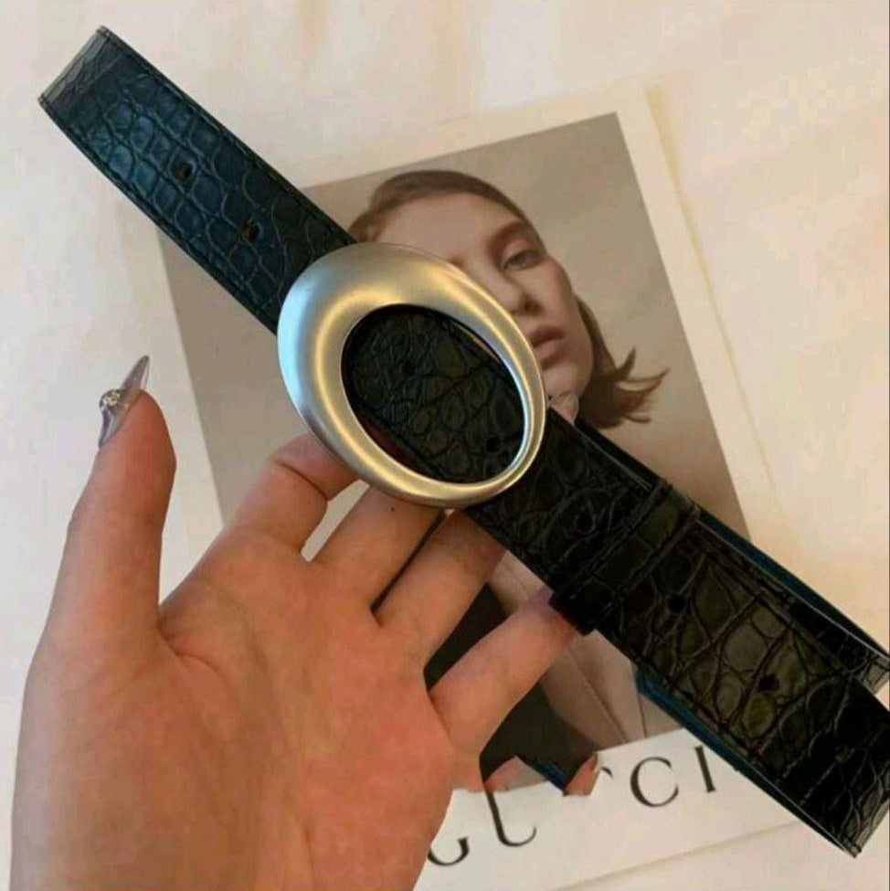 Black crocodile-patterned belt with silver buckle held by a hand on a magazine background