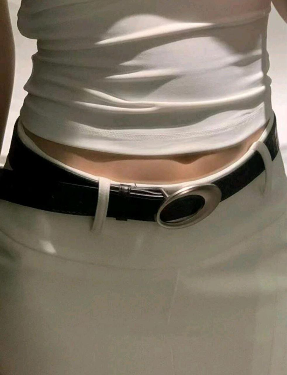 Close-up of a person wearing a white top and black belt with a large buckle.