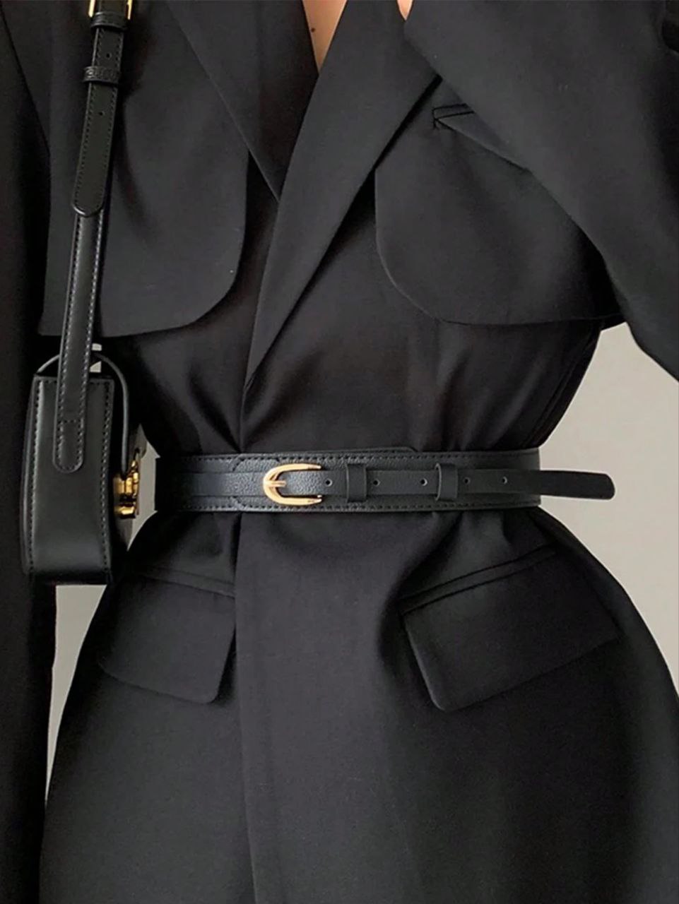 Black trench coat with a belt and black handbag on a neutral background