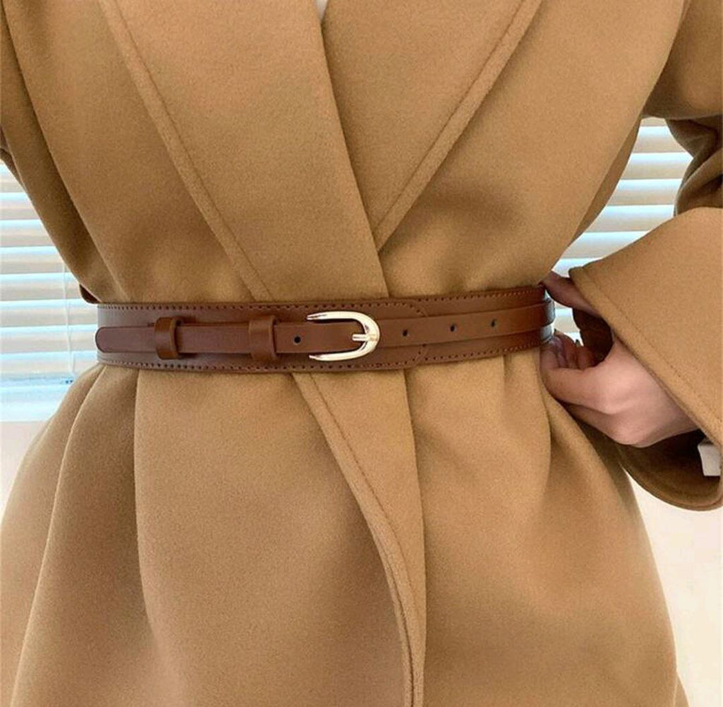 Tan coat with a brown belt being adjusted against a neutral background