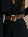 Person wearing a dark suit with a brown belt and gold buckle.