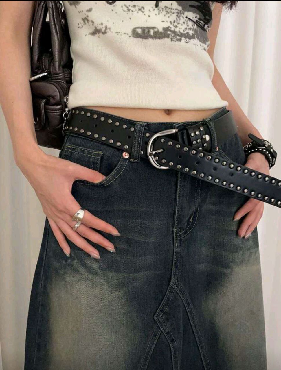 Girl wearing a black studded belt with a white top and dark jeans.