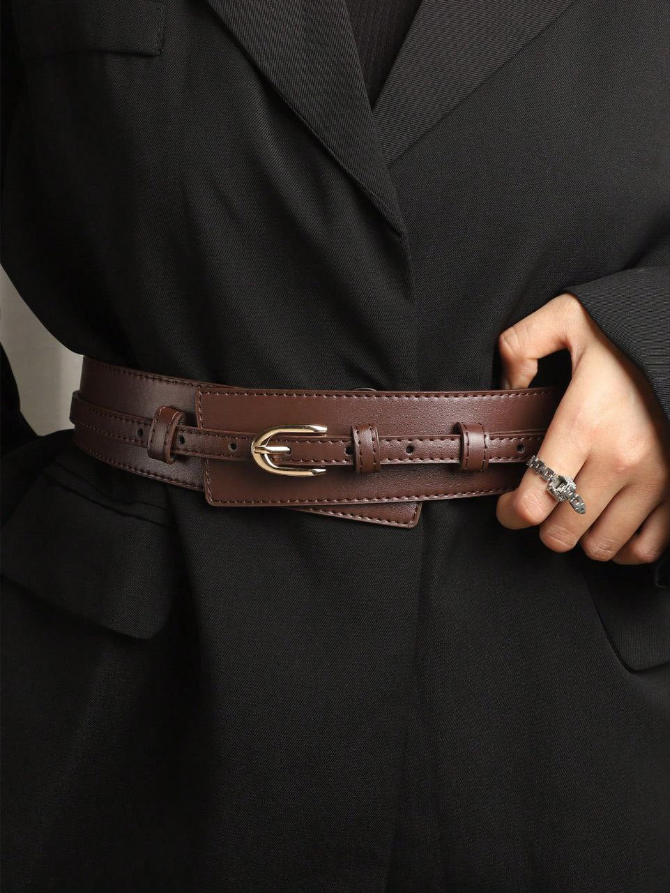 Person wearing a black coat with a brown leather belt with a gold buckle.