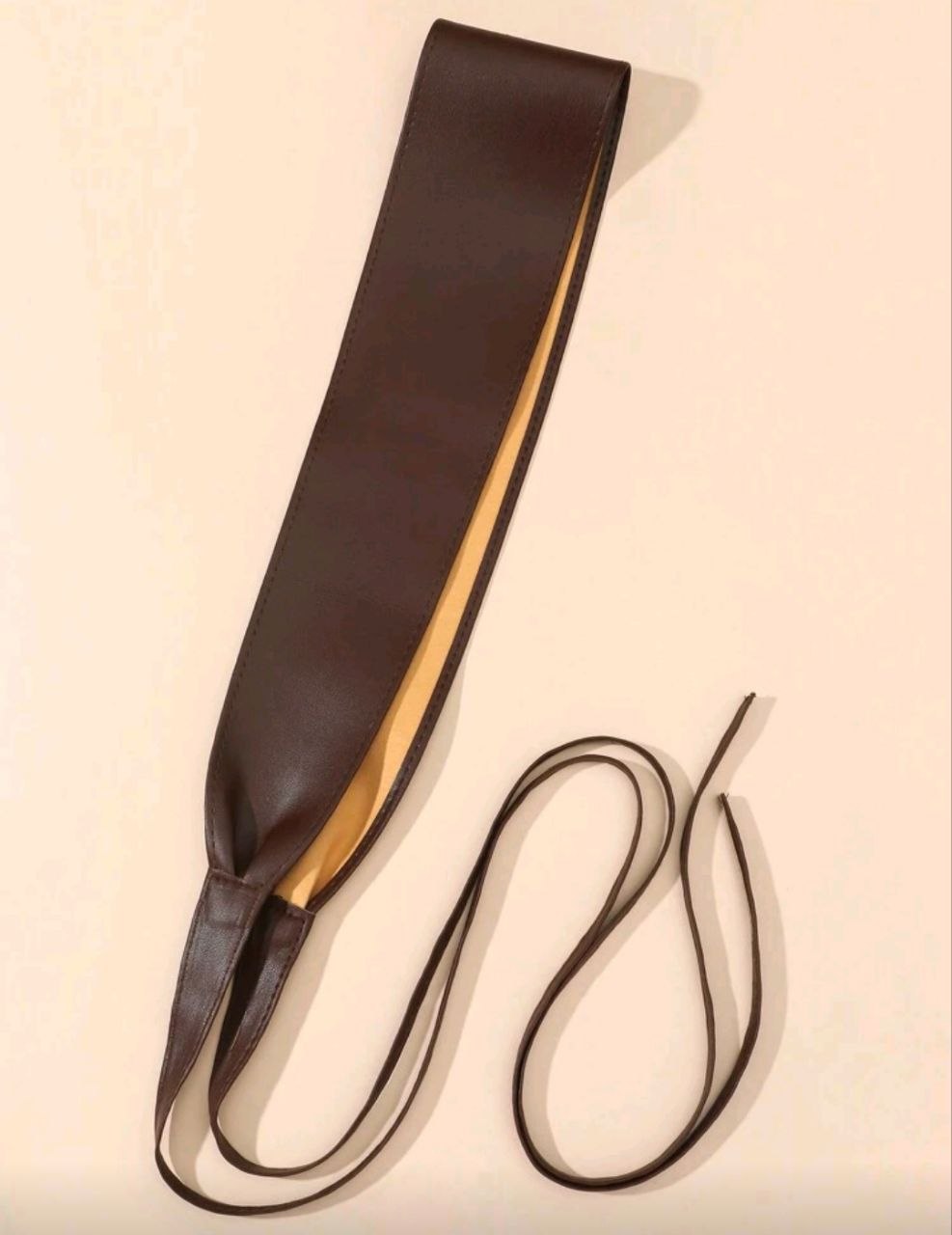 Brown leather belt with a strap on a beige background