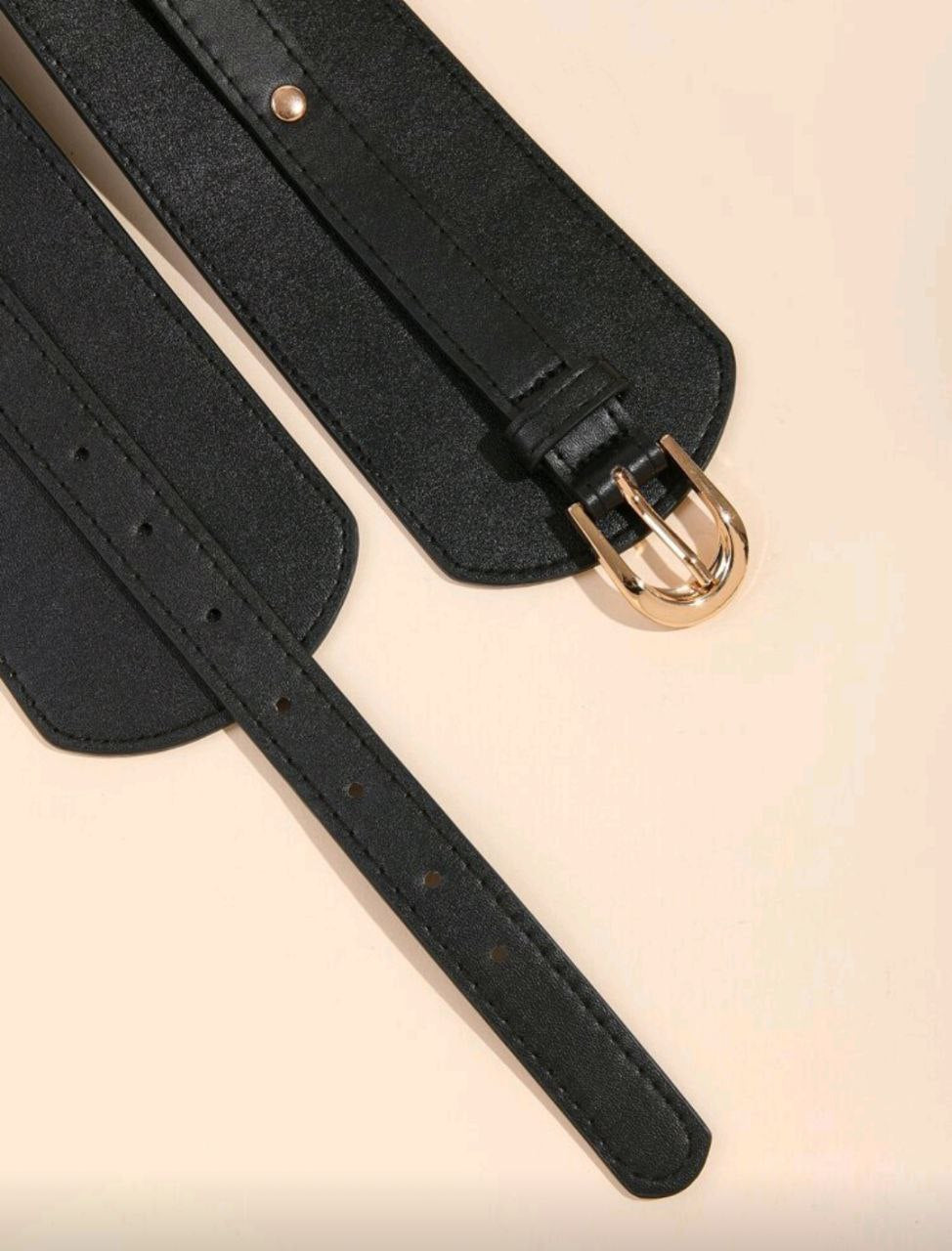 Black leather belt with gold buckle on a beige background