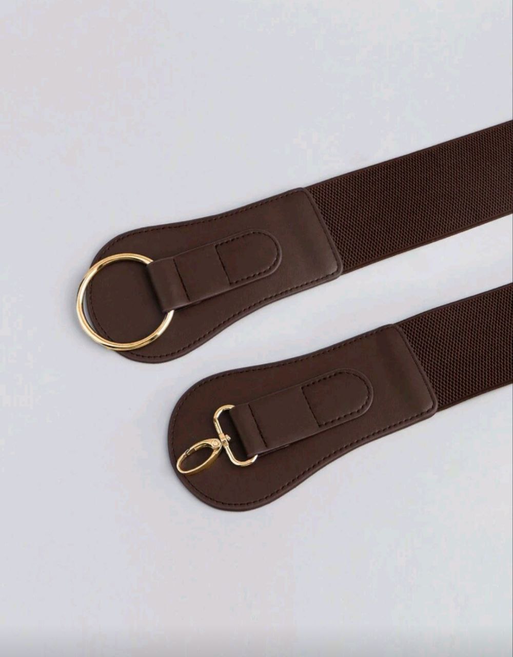 Brown belt with gold hardware on a light gray background