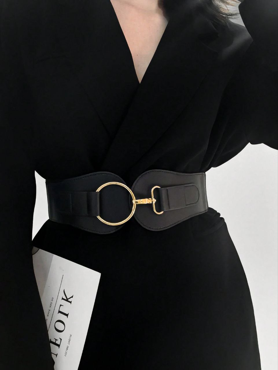 Person wearing a black outfit with a wide belt featuring a gold buckle on a white background
