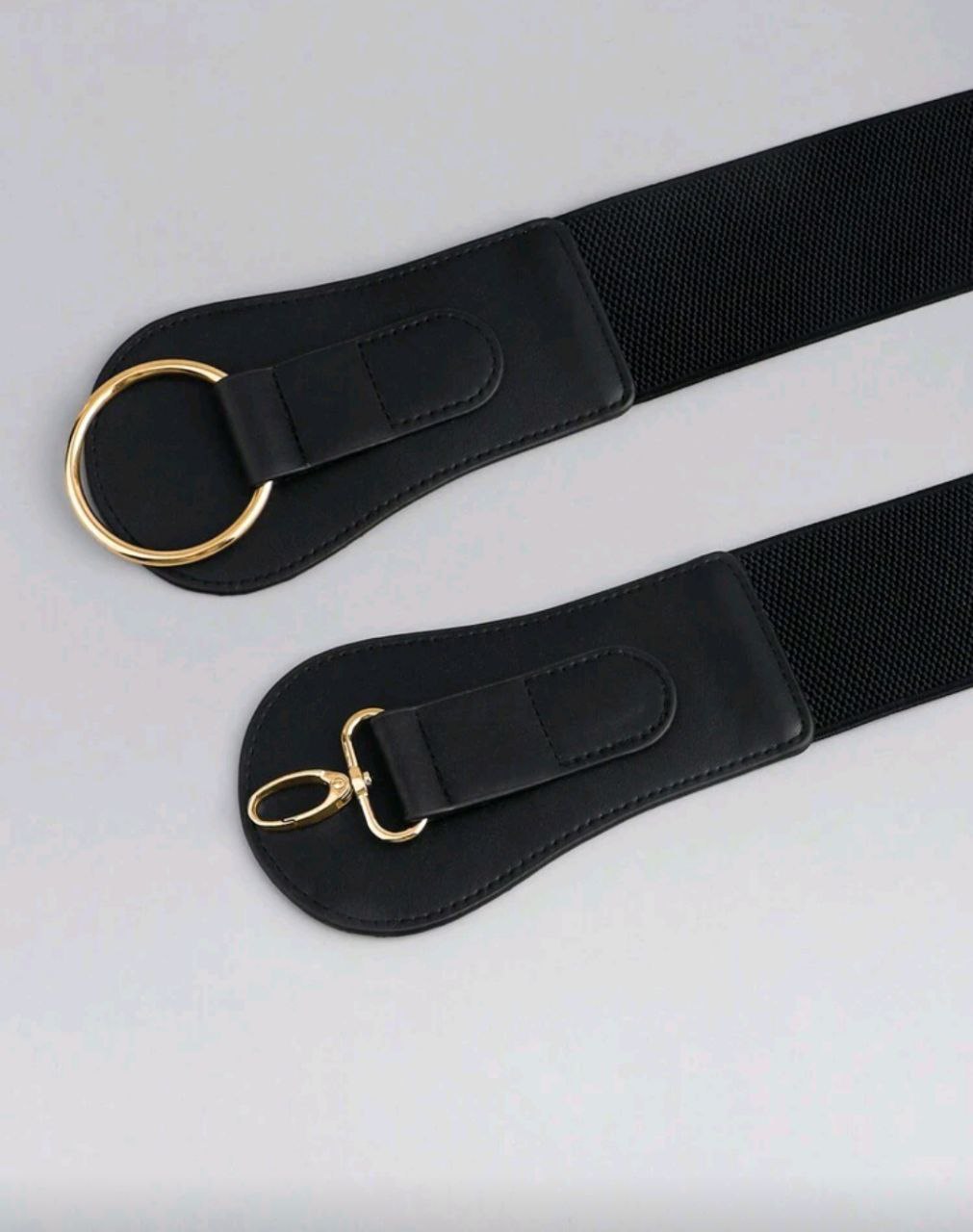 Two black straps with gold hardware on a light gray background