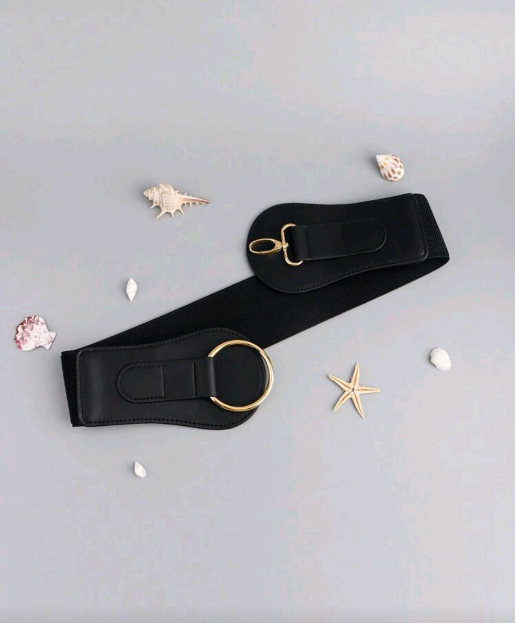 Black belt with gold hardware on a light gray background with decorative elements.