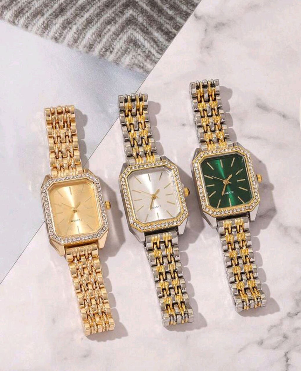 Three gold and silver watches with different colored faces on a marble surface.