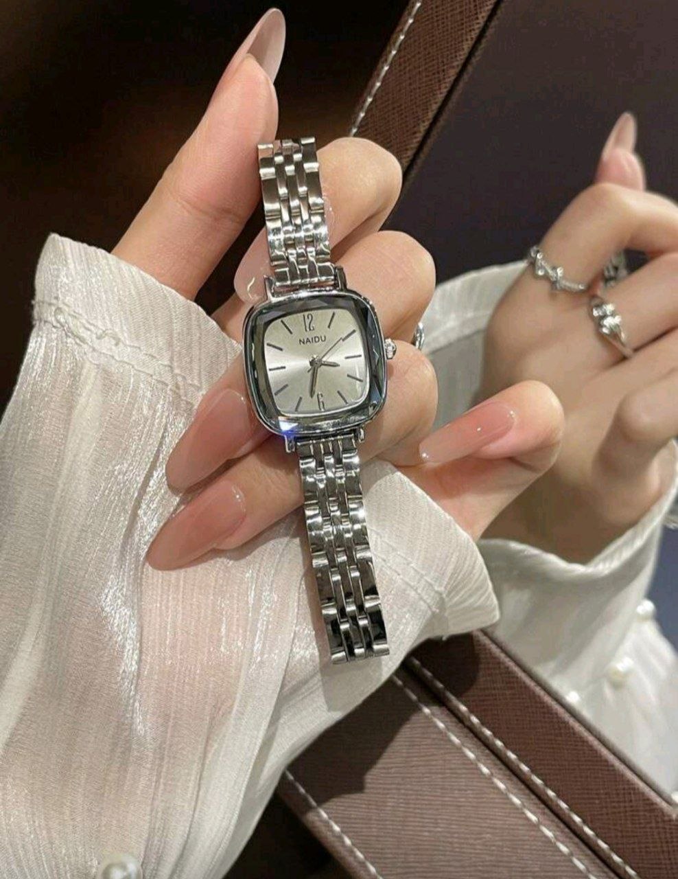 Silver watch held by a hand with a blurred background