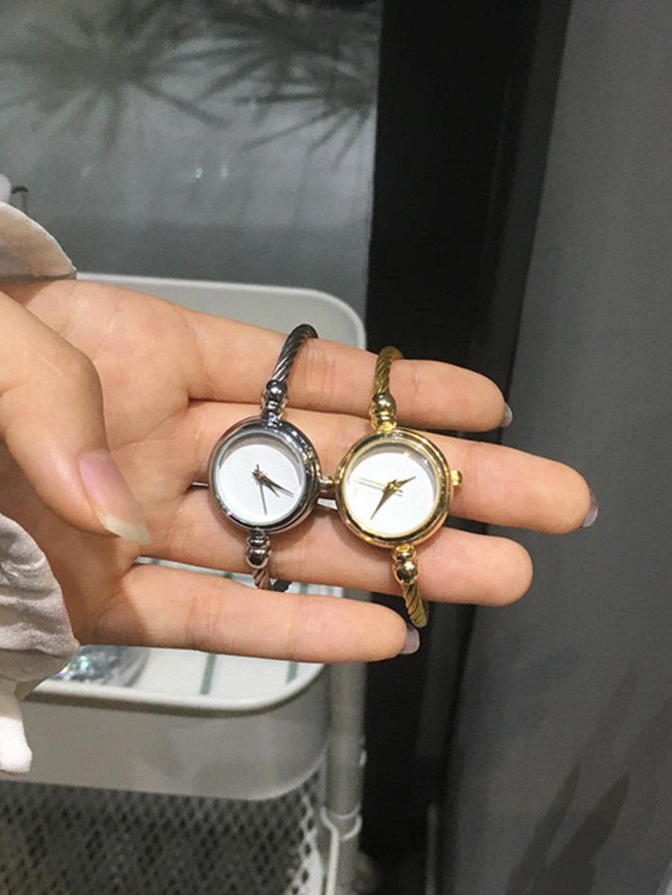 Two small wristwatches held in a hand against a dark background