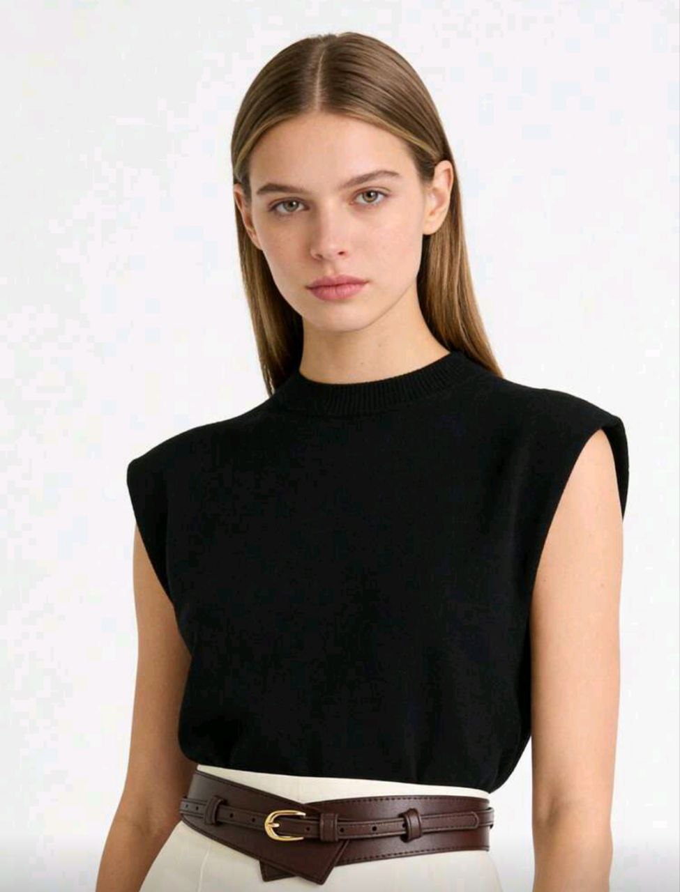 Woman wearing a black sleeveless top with a brown belt against a white background