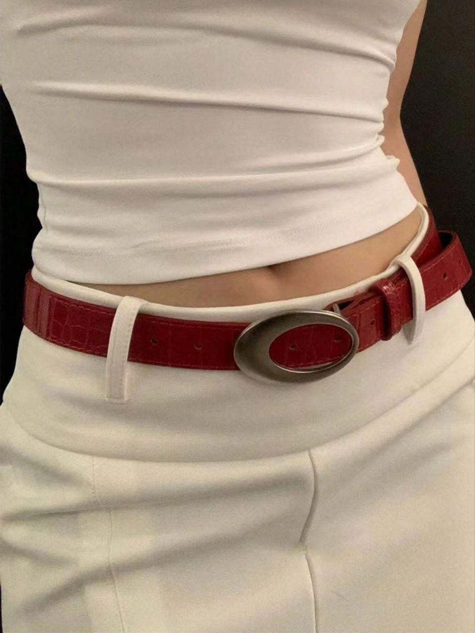 Red belt with a silver buckle worn by a person in a white shirt and pants.