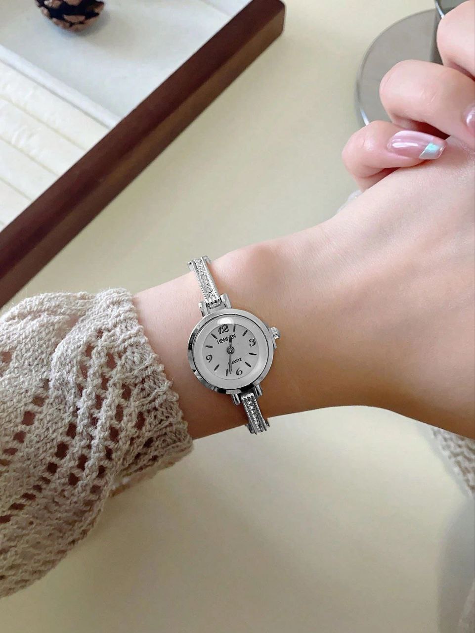 Silver wristwatch on a person's wrist with a neutral background